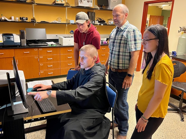 Fr. Michael Antonacci (seated) points to data on the computer screen as (from left) Tony Sparta, Dr. Jason Vohs and Angelina Bucci look on.